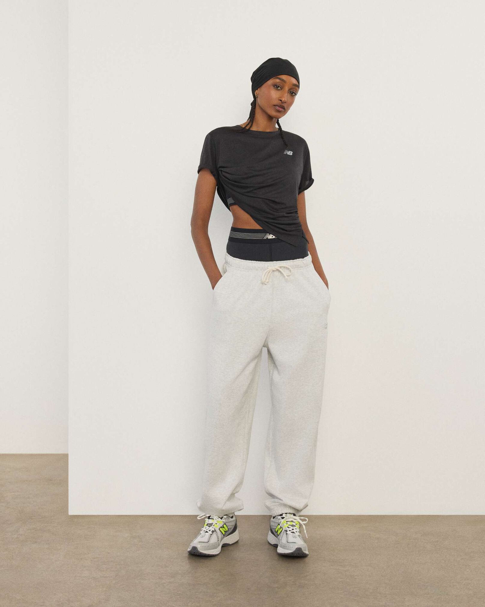 A woman wearing New Balance standing in front a white wall.