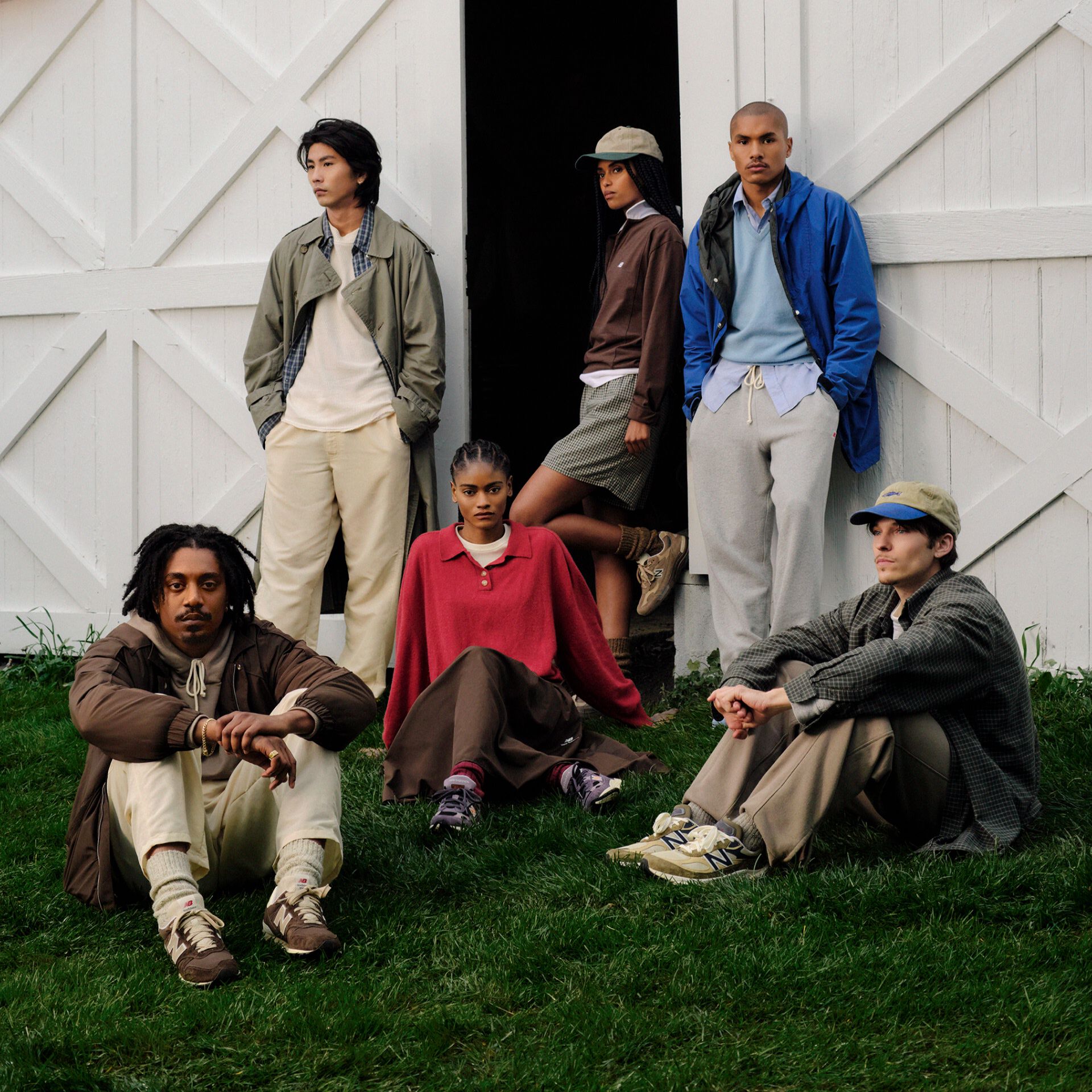 A group of 6 people all wearing New Balance Made in USA apparel and sneakers sitting and standing in front of white barn doors with grass in front.