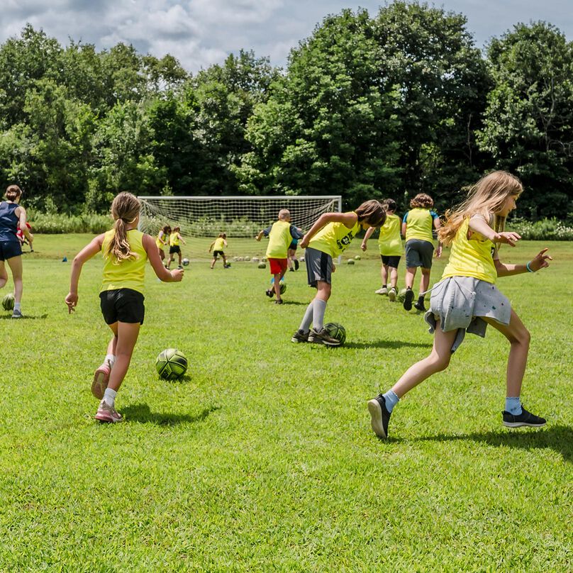Several light-skinned children practicing soccer skills on a field.
