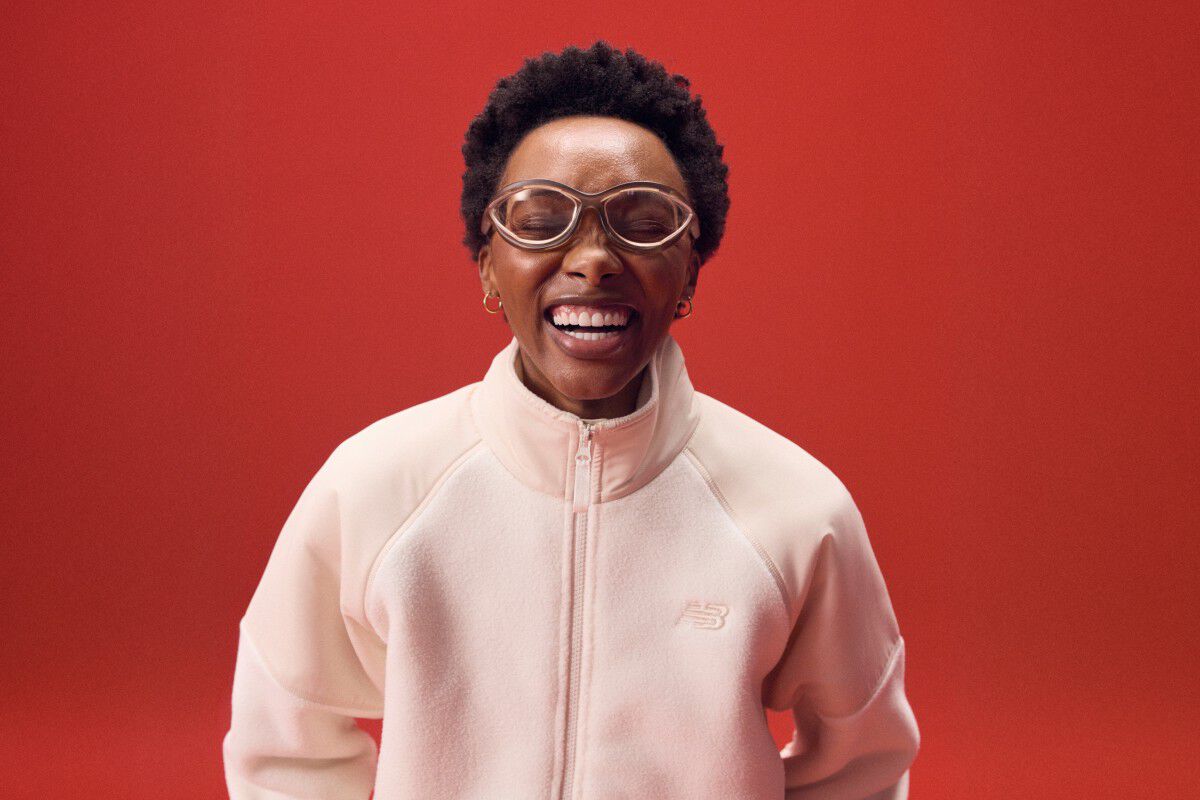 Woman laughing while wearing a pink zip-up on a red background.