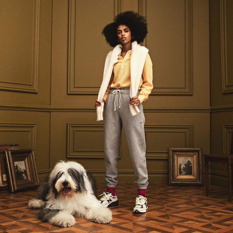Woman standing in a beautiful indoor environment wearing MADE in USA sweatpants and footwear. There is a large dog laying down next to her.