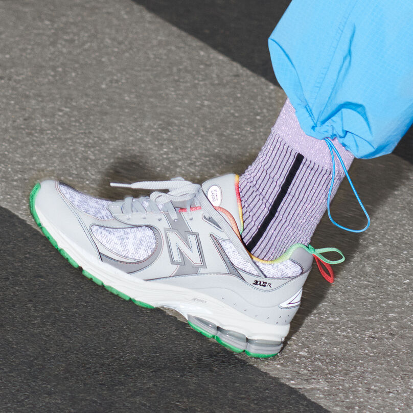 Knee down, side profile of a person stepping on a road, wearing the grey GANNI 2002R shoe, light purple socks and blue pants