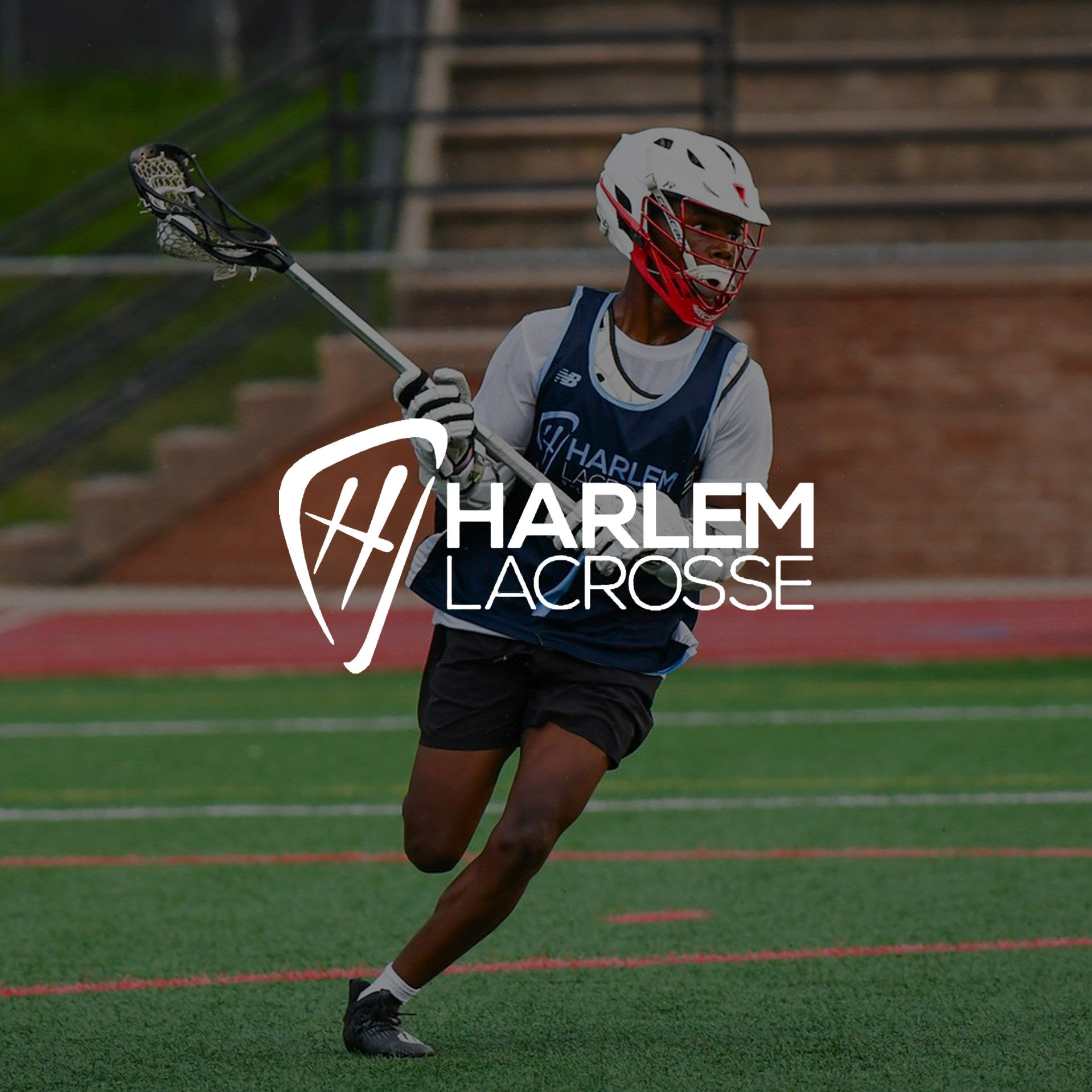 A dark-skinned, uniformed teen male-presenting student athlete running down the field holding a lacrosse stick.