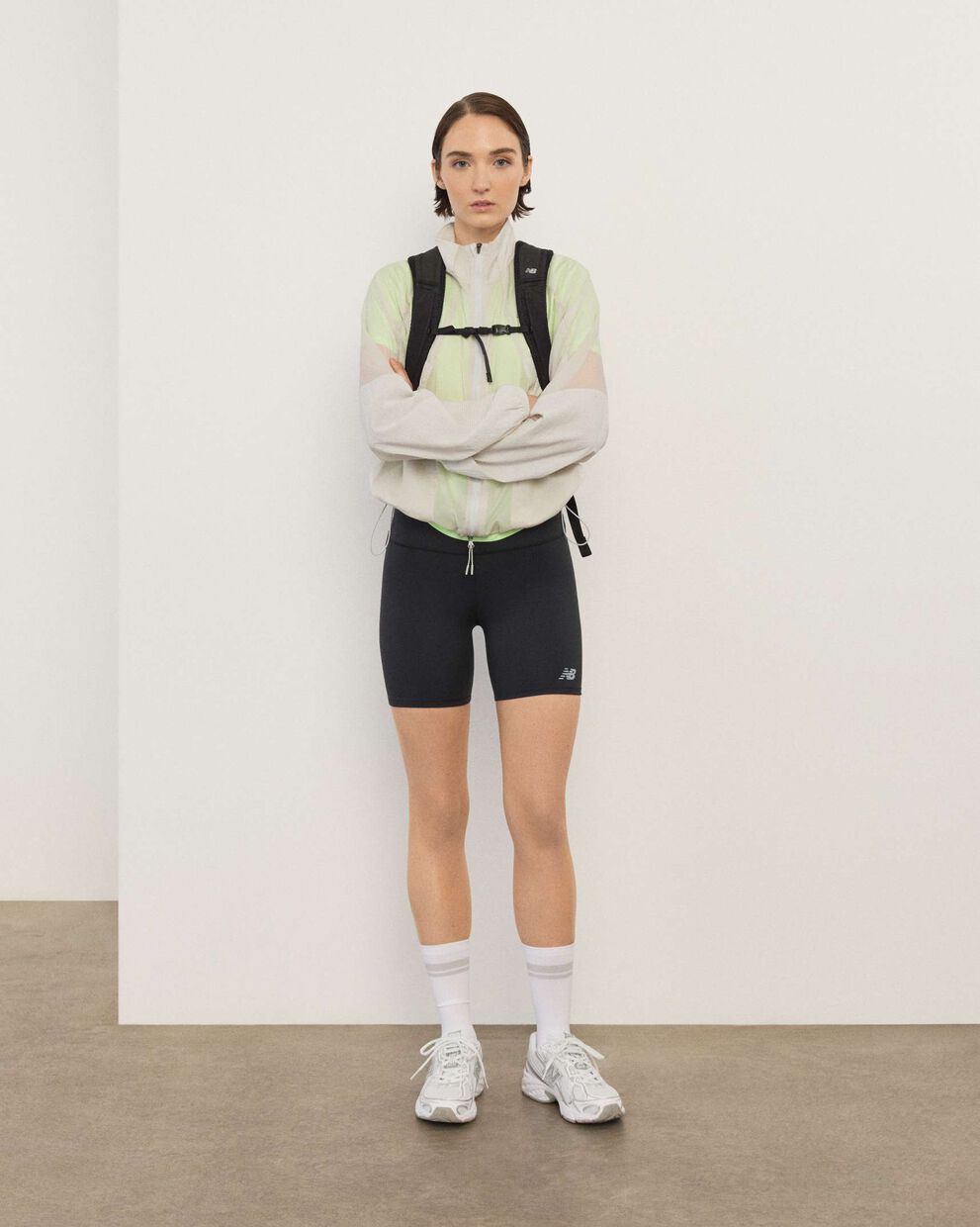 A woman wearing New Balance standing in front a white wall.