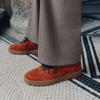 Knee down view of a man wearing a pair of New Balance Made in UK sneakers standing on a patterned tile floor.  